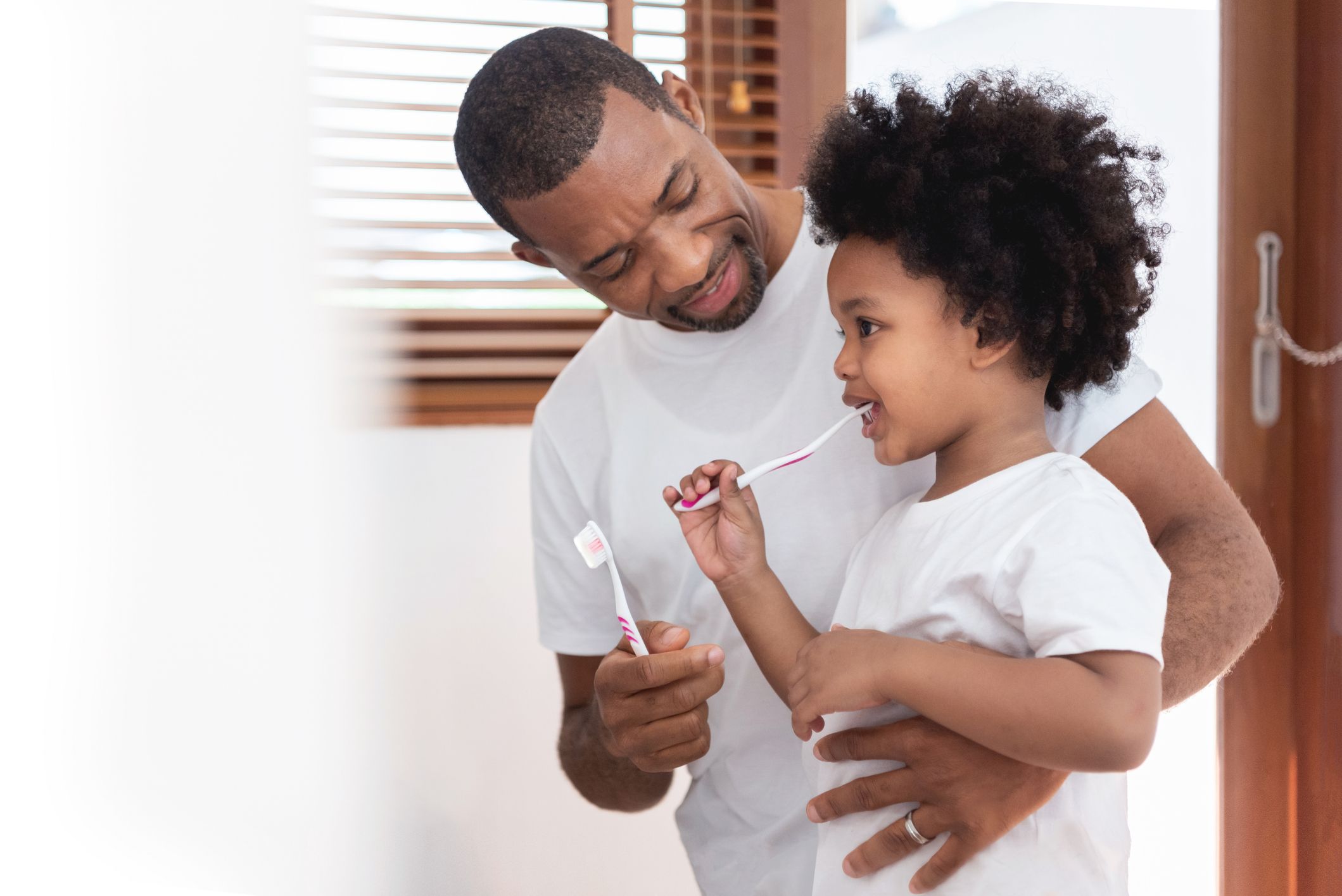 Father supports son in practicing good dental hygiene at home.